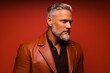 © Iigo - Handsome senior man with long gray beard and mustache wearing a leather jacket on red background