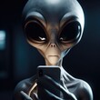 A grey-skinned alien with large, black, almond-shaped eyes holding a smartphone close to its face. The alien has a slender and elongated head, with prominent cheekbones and no visible nose or ears