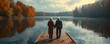 aged couple admiring autumn lake from pier Romantic couple with arms up sitting on old wooden pier at lake, sunset shot