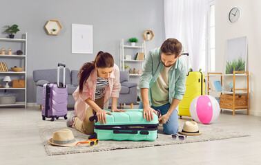 Portrait of a young couple man and woman packing suitcase for vacation trip sitting on the floor at home together. Family summer holiday preparations. Travelling and journey concept.