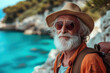 © Sergio - Senior male traveler with a beard in a hat and sunglasses posing confidently on the seashore