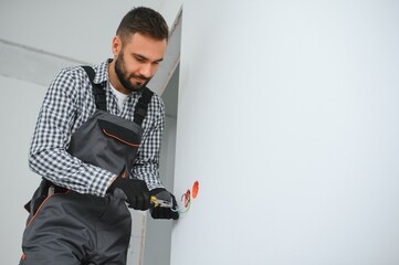 Electrician Builder at work, installation of sockets and switches. Professional in overalls with an electrician's tool. Against the background of the repair site