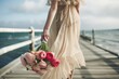 woman in a maxi dress and a bouquet of ranunculus strolling on a pier