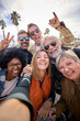 © CarlosBarquero - Vertical group diverse cheerful middle-aged tourist friends posing smiling taking photo selfie embracing together with front camera on travel outdoor. Mature happy six people enjoy holidays sunny day