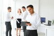 © Serhii - Portrait of smiling indian businessman standing in modern office on colleagues background
