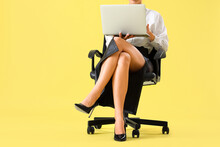 Businesswoman With High Heels Using Laptop In Office Chair On Yellow Background