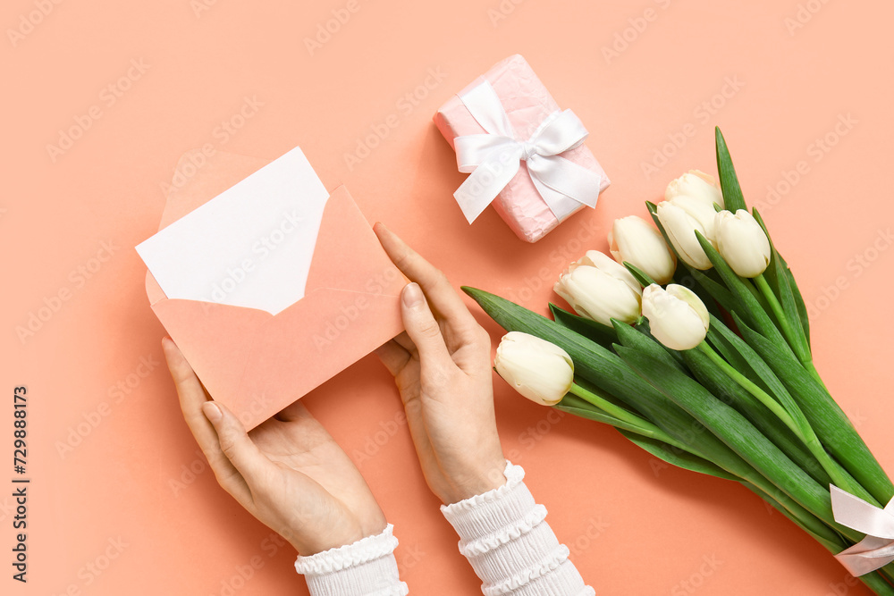 Female hands with envelope, gift box and white tulips on orange background