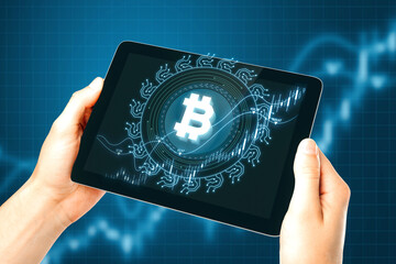 Poster - Close up of businessman hands holding tablet with creative glowing bitcoin on dark blue background with candlestick. Cryptocurrency, digital money and economic network concept.