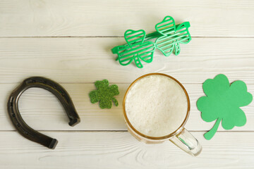 Mug of beer with paper clovers, plastic eyeglasses and horseshoe on white wooden background. St. Patrick's Day celebration