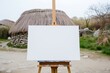empty canvas on easel before a reconstructed neolithic home