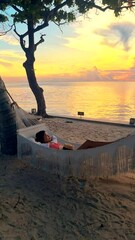 Wall Mural - women watching the sunrise in a hammock on a tropical beach in Hua Hin Thailand. Asian women in a hammock on the beach of Huahin Thailand