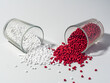 hot cut type red and white masterbatch granules spilled from a shot glass on a white background, this polymer is a coloring agent for products in the plastics industry