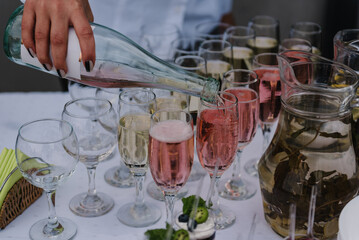 The waiter woman pouring sparkling wine. Catering service concept. The female pours champagne into flute glasses. Champaign is being poured into glasses. Bottle in a closeup view. Rows of full glasses