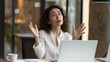 © mikeosphoto - A businesswoman a white blouse sitting at a desk with laptop in a modern office space. Woman in the middle of a conversation or a meeting gestures with her hands raised, palms up