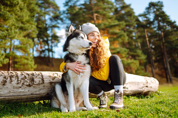 Wall Mural - Beautiful young woman in a yellow coat walks in a park with her pet husky. A pet owner spends time with her dog. Concept of fun, entertainment.