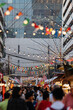 A vibrant market street in Bangkok under a canopy of colorful lights and flags, bustling with activity.