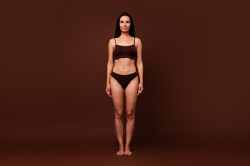 Poster - Unfiltered full length photo of natural thin body positive brunette girl standing in studio isolated on dark brown color background