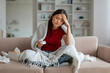 © Prostock-studio - Ill asian woman with headache sitting on couch at home,