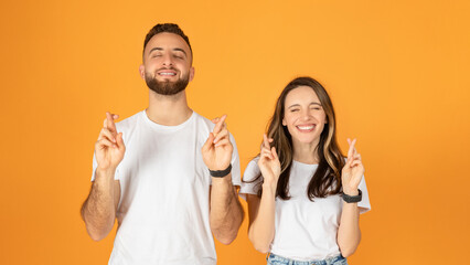 Poster - Joyful young couple with eyes closed, fingers crossed for good luck