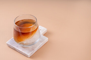 Wall Mural - Cognac or whiskey with ice, strong alcohol cocktail with frozen glass on light beige background copy space