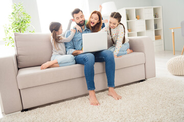 Poster - Full size photo of four people guy closed eyes sit on couch crazy funky girls use laptop hand pull dads ear indoors