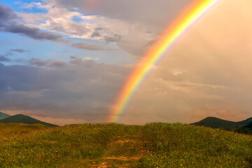  Colorful rainbow after rain over green hills in the mountains.