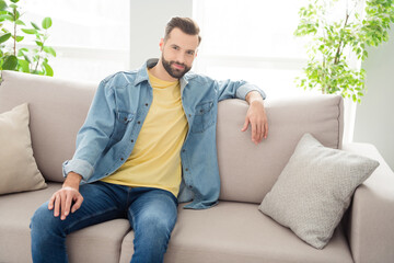 Wall Mural - Photo portrait of brunet sitting on sofa wearing jeans outfit smiling chilling on holiday