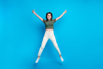 Poster - Full size photo of good mood lovely woman wear green t-shirt white trousers jumping raising hands up isolated on blue color background