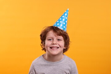 Birthday celebration. Cute little boy in party hat on orange background