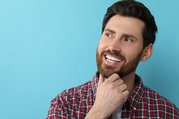 Canvas Print - Portrait of smiling man with healthy clean teeth on light blue background. Space for text