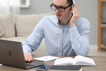 Wall Mural - E-learning. Young man using laptop during online lesson at table indoors.