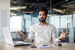 © Tetiana - Indian businessman meditating at office desk with laptop for mindfulness
