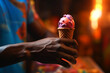 close-up of an African American hand presenting a vibrant purple scoop of ice cream in a classic waffle cone, illuminated by the golden hues of twilight