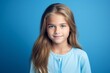 Portrait of a beautiful little girl with long blond hair. Blue background.