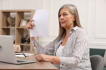 Poster - Menopause. Woman waving paper sheet to cool herself during hot flash at wooden table indoors