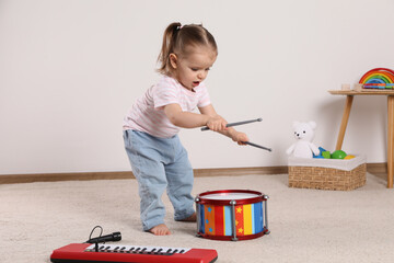 Wall Mural - Cute little girl playing with drum, drumsticks and toy piano at home