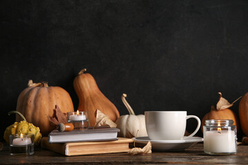 Wall Mural - Cup of tea, books, autumn leaves, burning candles and pumpkins on table near black wall