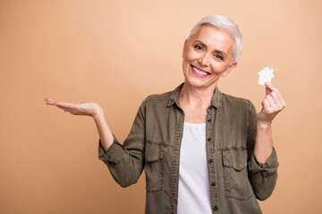 Canvas Print - Portrait of holding miniature house toy mature woman realtor promoting new apartments with discount isolated on beige color background