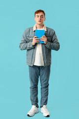 Wall Mural - Surprised young man holding book on color background