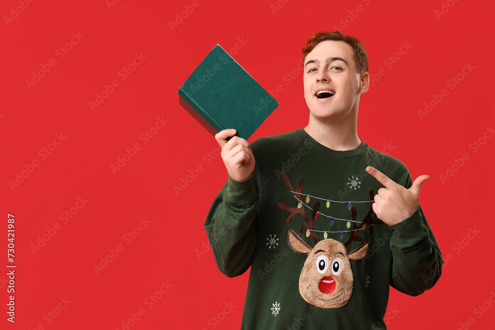 Emotional young man pointing at book on red background