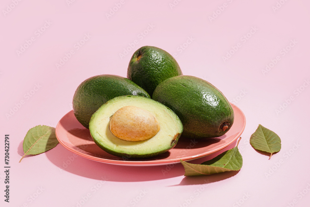 Plate with fresh ripe avocados and leaves on pink background