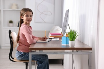 Poster - E-learning. Cute girl taking notes during online lesson at table indoors