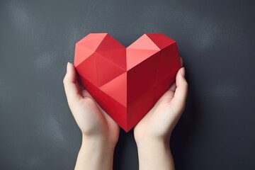 Female hand holding polygonal paper red heart on gray background, copy space, Valentine's day, Mother's day, Women's Day and love concept