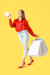 Sticker - Happy young woman with gift card and shopping bags on yellow background