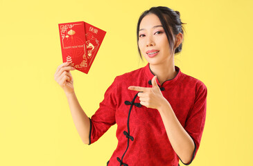 Wall Mural - Young Asian woman pointing at envelopes on yellow background. Chinese New Year celebration