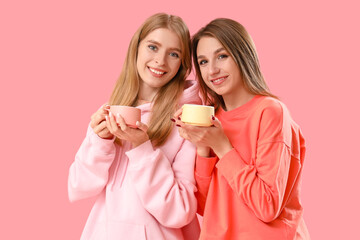 Wall Mural - Beautiful young women with cups of tea on pink background