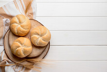 Board with delicious kaiser rolls and wheat ears on white wooden background