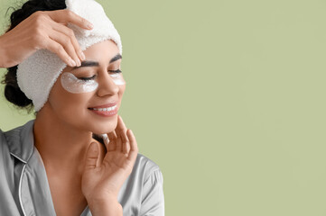 Wall Mural - Young African-American woman in headband with under-eye patches on green background, closeup