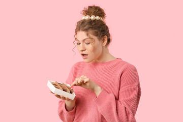 Sticker - Beautiful young woman holding box with sweet chocolate candies on pink background