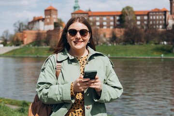 Wall Mural - Beautiful stylish woman walking on spring day and holding mobile phone on the street background. Phone Communication. Urban lifestyle concept. Check social networks, send sms